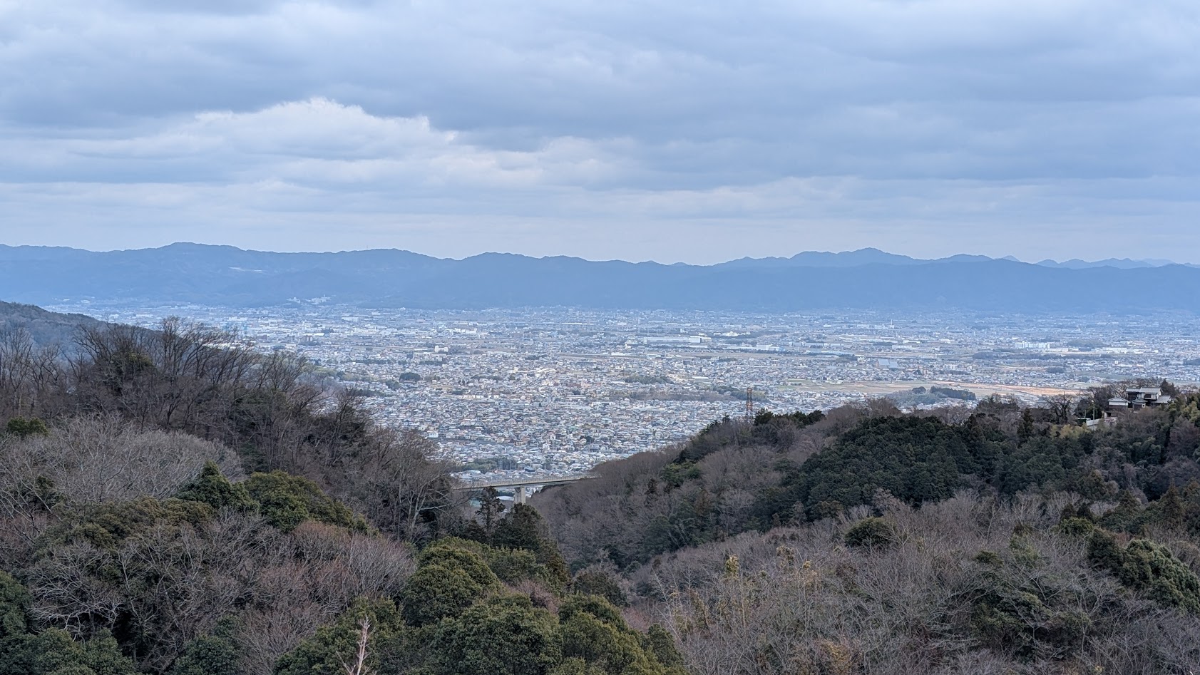 信貴山朝護孫子寺の本堂舞台から見下ろす奈良盆地の全景。遠くに奈良の街並みが広がり、手前には境内の山々の緑が見える。