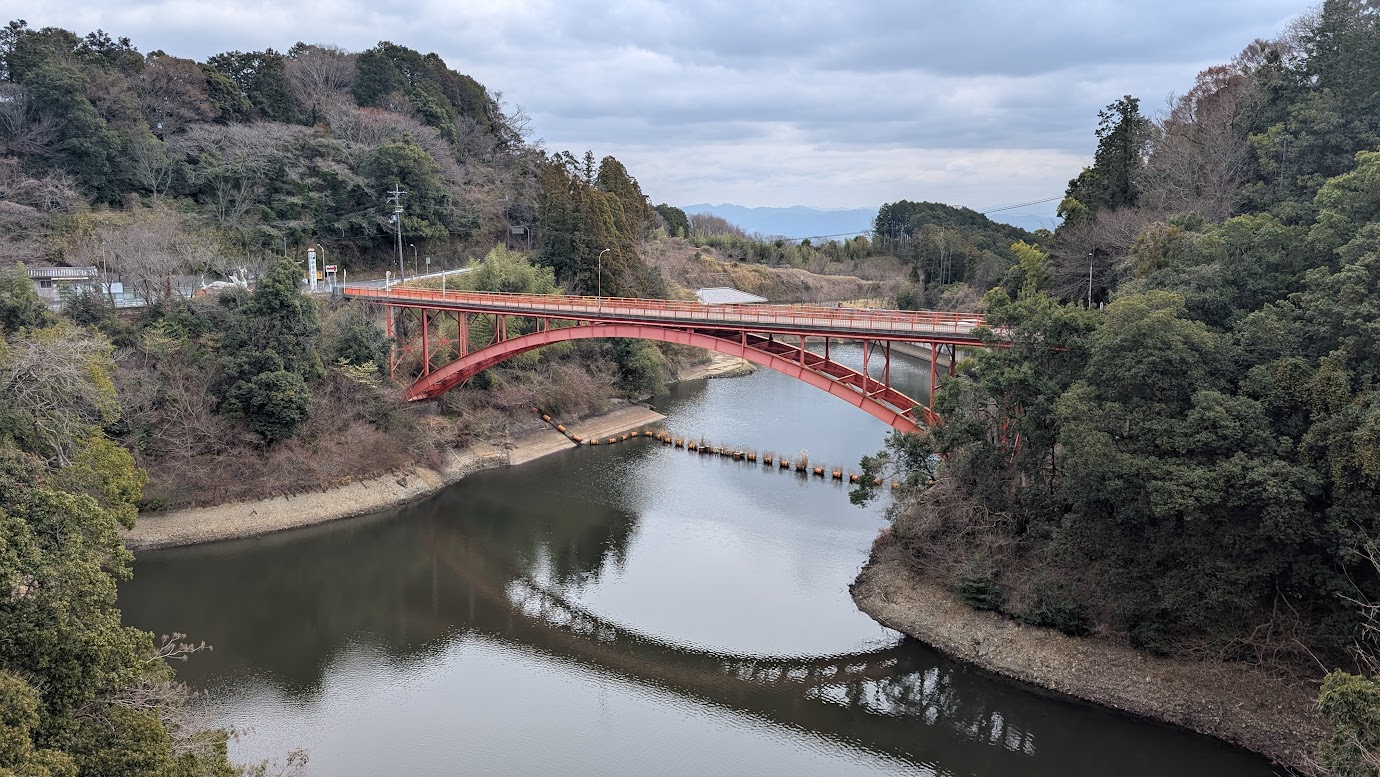信貴山朝護孫子寺の「開運橋」上から見た景色。深い渓谷に架かる鮮やかな朱色の橋と、その下に広がる大和平野、そして周囲を囲む緑豊かな信貴山の山並みが一望できる。