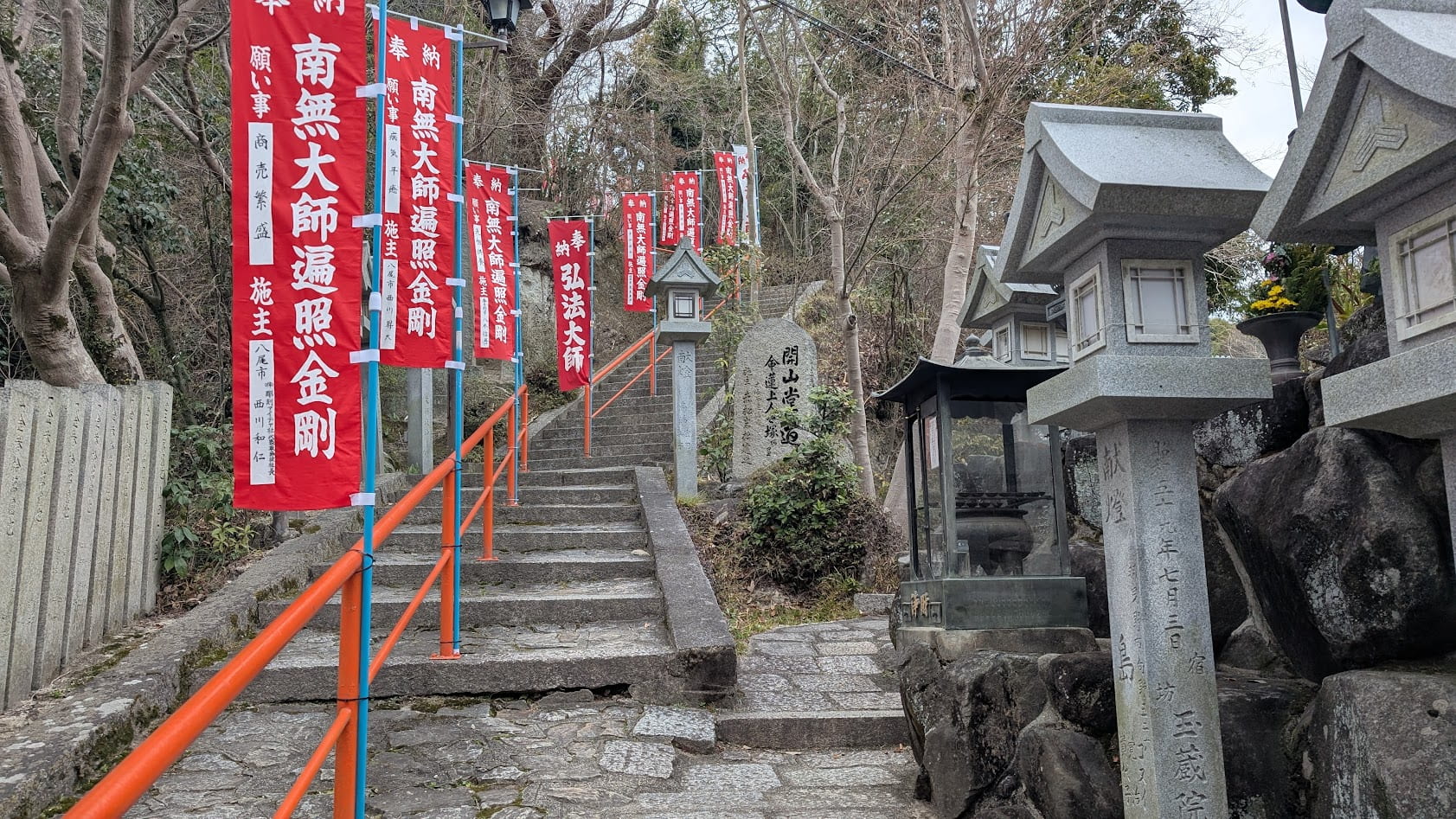 信貴山朝護孫子寺の開山堂へと続く、急で長い石階段。両脇には石灯籠が並び、周囲は深い緑の木々に覆われている。