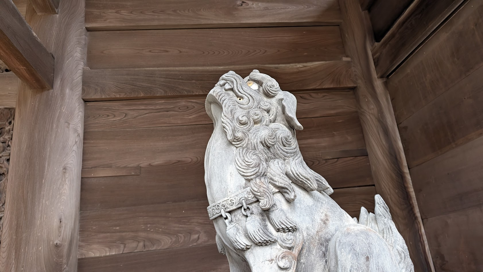 信貴山朝護孫子寺・仁王門の裏側に配置された狛犬の吽形(うんぎょう)。口を閉じた「吽(うん)」の表情で、木造の静かな質感と威圧的な眼差しが際立つアップ。