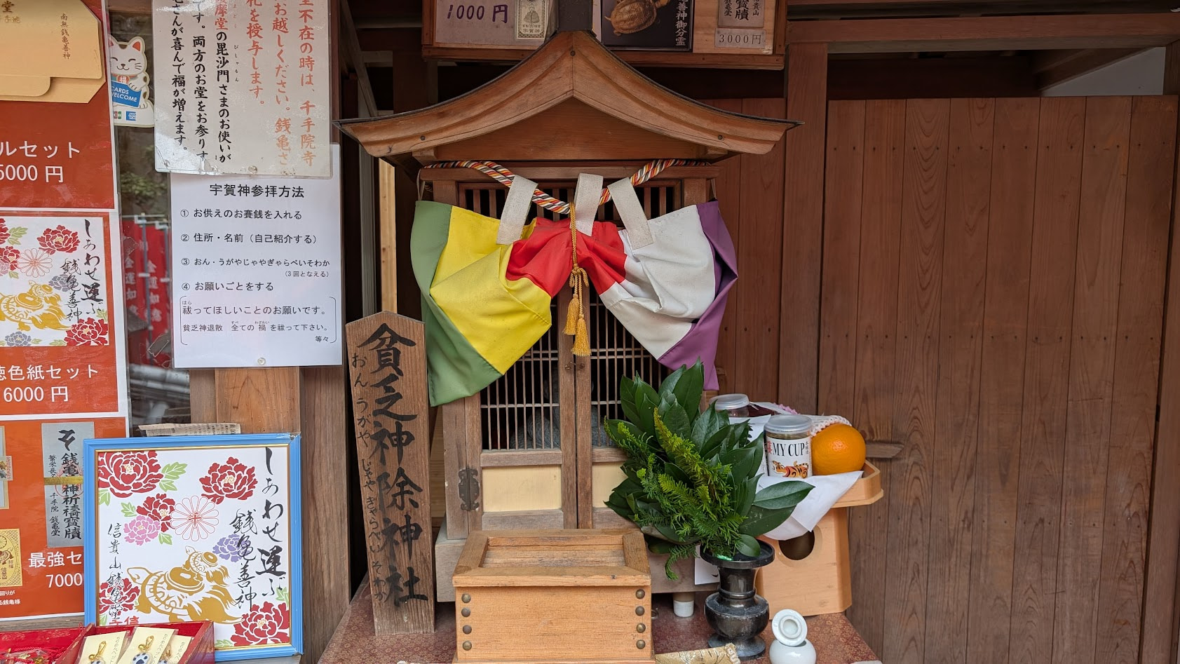 信貴山朝護孫子寺・千手院の銭亀堂横にある「貧乏神除神社」。小さな社に赤い幟が立ち、周囲には「貧乏神除け」の文字が見える。