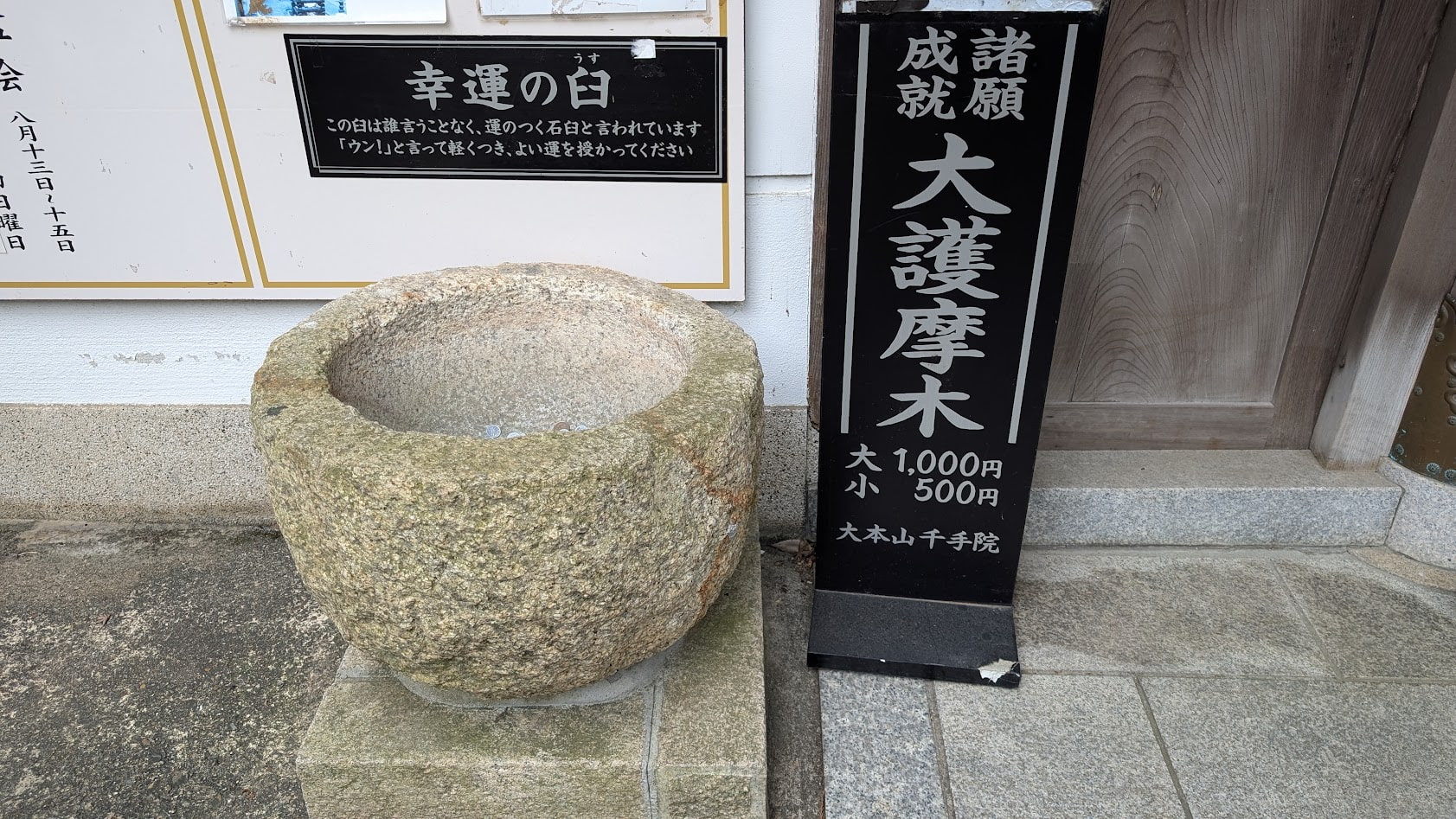 信貴山朝護孫子寺・千手院の建物脇にある「幸運の臼」。石造りの臼の上に説明書きがある。この臼は誰言うことなく、運のつく石臼と言われています。