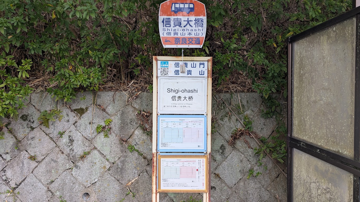 信貴大橋のたもとにあるバス停。朱色の欄干が美しい信貴大橋の入り口付近に位置し、背後には信貴山の緑豊かな山々が広がっている。