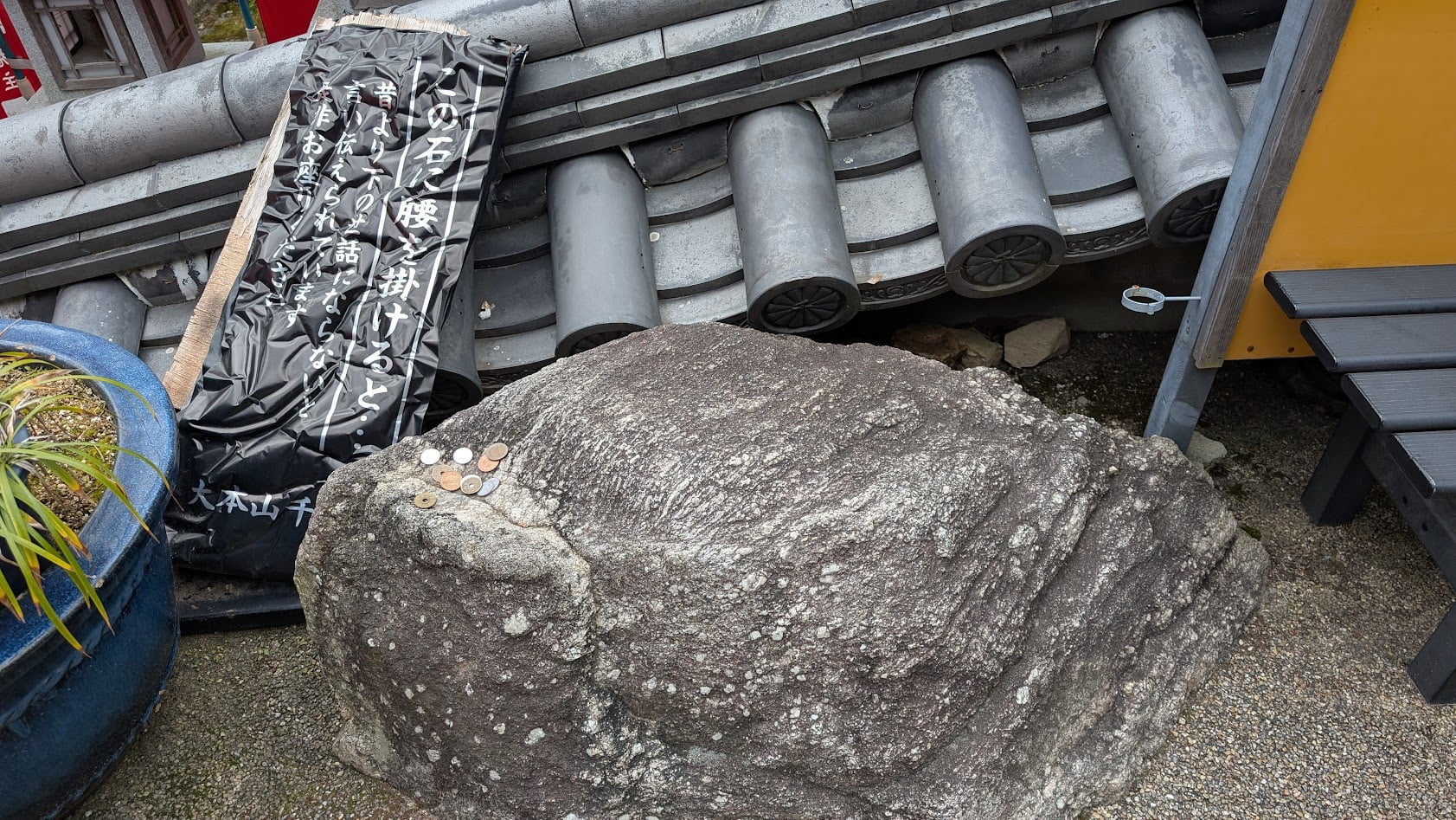 信貴山朝護孫子寺・銭亀堂にある腰掛石。傍らには「この石に腰かけると昔より下の人に世話にならないと言い伝えられています」という趣旨の説明書きが添えられている。