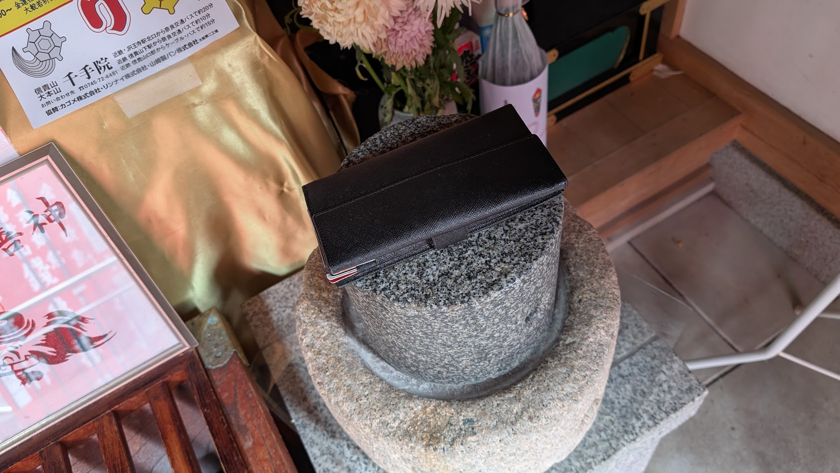 信貴山朝護孫子寺・銭亀堂の「黄金の臼」の上に、参拝者が自分の財布を乗せた様子。財布の下には「壱億円札」の札が見え、臼の周囲には銭亀善神の幟が並ぶ。