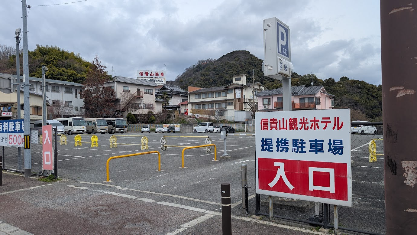 信貴山観光ホテル提携の駐車場入口。完全に舗装され、白線で区画が仕切られている。入口には料金システムのゲートバーと、1日500円の案内板が設置されている。