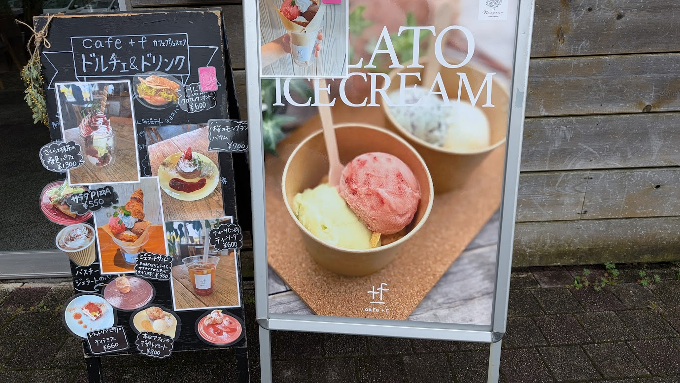 馬見丘陵公園内のカフェ「Cafe. +f」の店頭看板。春限定のさくらパフェや桜モンブラン、本格的なジェラート、サラダピザなどのメニューが写真付きで紹介されている。
