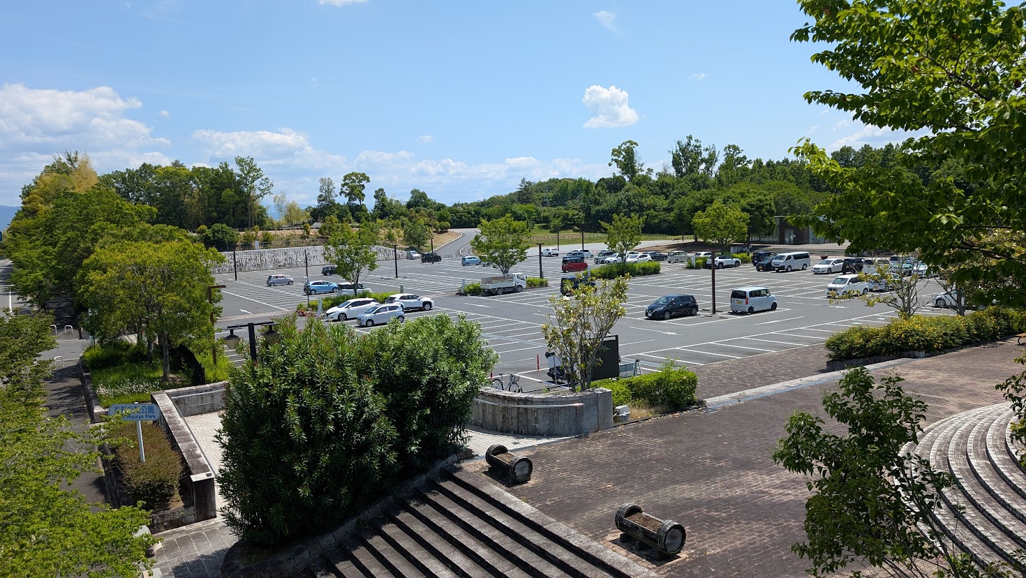 5月25日の平日13時に撮影した馬見丘陵公園北駐車場の混雑状況。広大な駐車スペースに車が点在している様子。