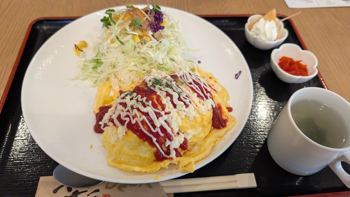大和郡山市の「彩食キッチン Bon」の「ぷりたまごのオムライス」。ふんわりとしたオムライスにデミグラスソースがかけられ、横にはレタスやトマトのサラダ、副菜、スープが添えられたワンプレート。