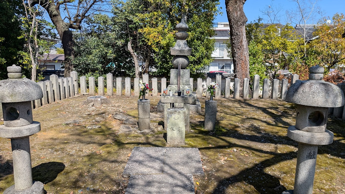 奈良県大和郡山市にある大納言塚（豊臣秀長の墓）。中央に大きな五輪塔が立ち、周囲には石灯籠や石柱、豊かな緑に囲まれた静かな空間が広がっている。