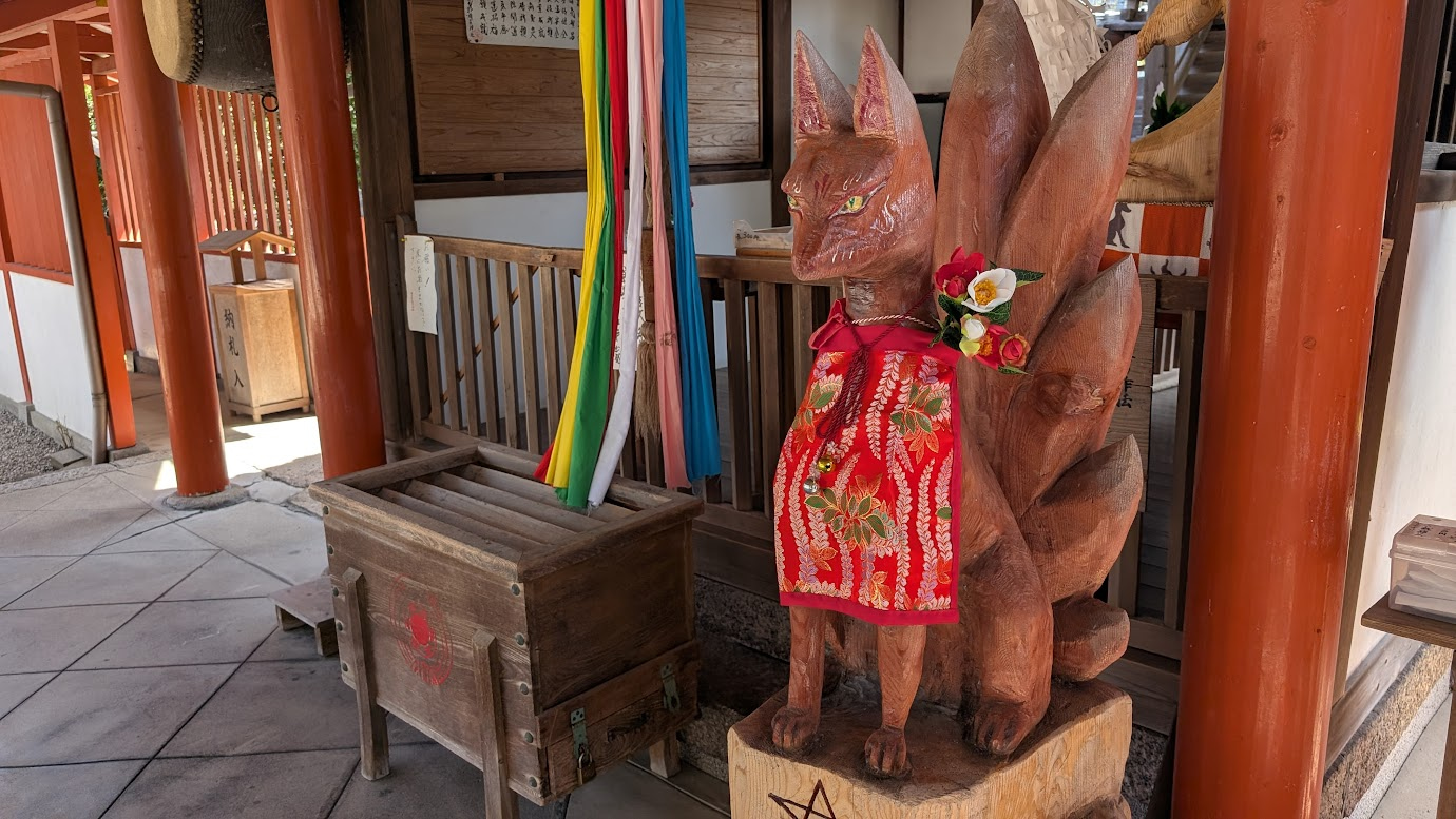 奈良県大和郡山市の源九郎稲荷神社、拝殿内に祀られた木造のお狐様（狛狐）の置物。長く垂れた眉と柔和な表情が特徴で、台座には「源九郎」の文字が記されている。
