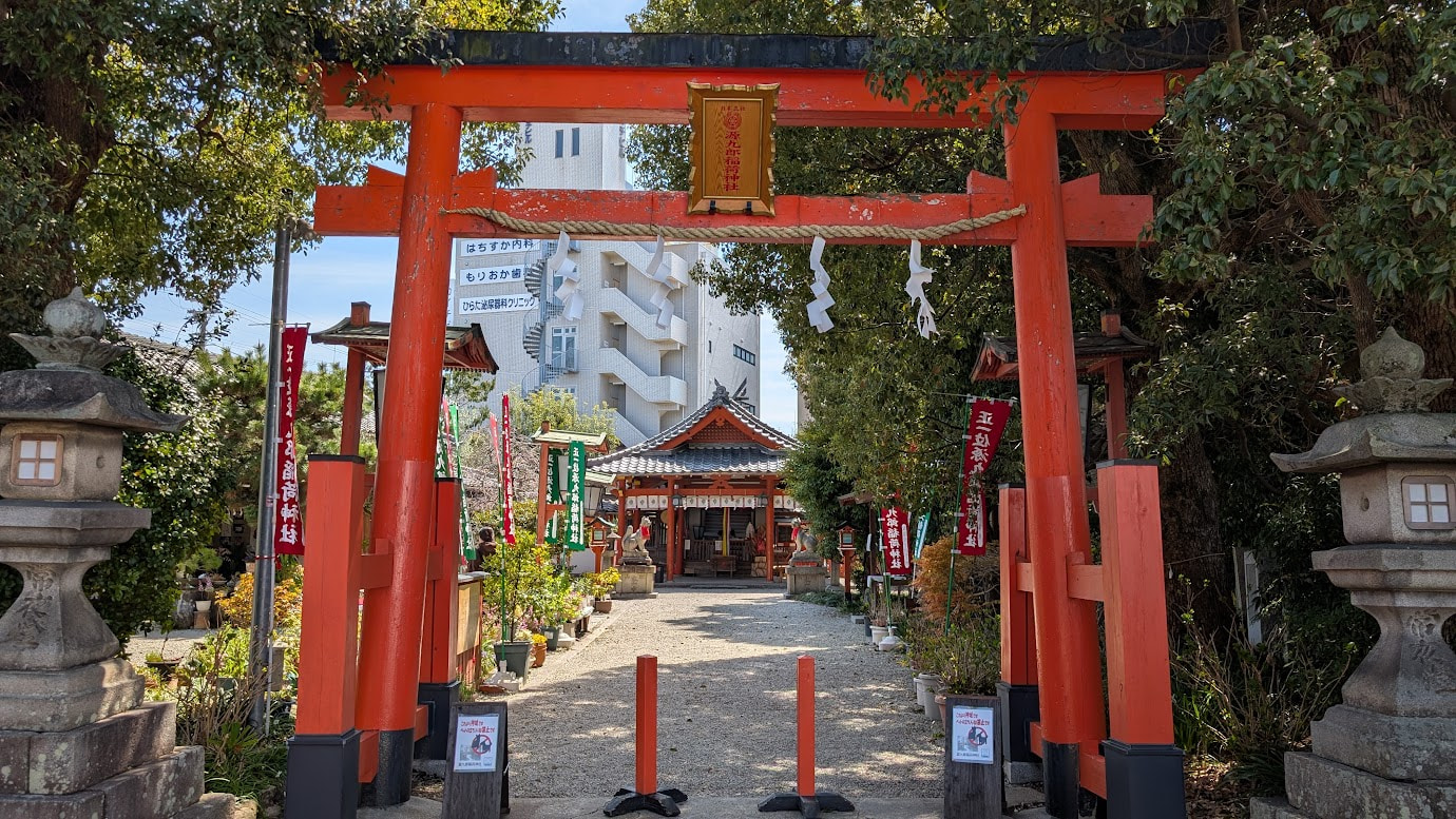 奈良県大和郡山市の源九郎稲荷神社。朱色の「源九郎稲荷大明神」の幟が参道に並び、奥には木造の拝殿と、その左右に狐の像（狛狐）が祀られている。
