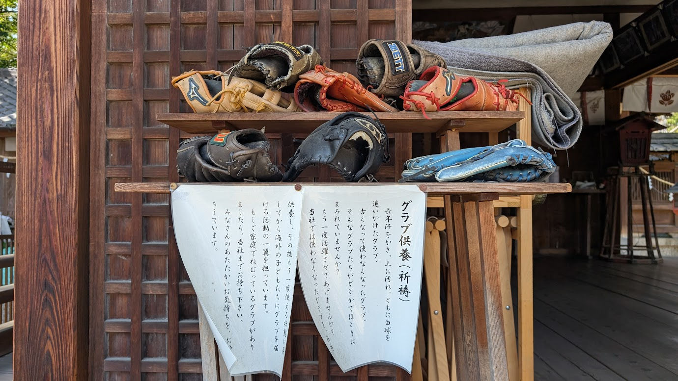 奈良県大和郡山市の郡山八幡宮に並べられた「グラブ供養」の野球グローブ。案内板には供養の趣旨と、海外の子どもたちへ寄贈する活動が記されている。