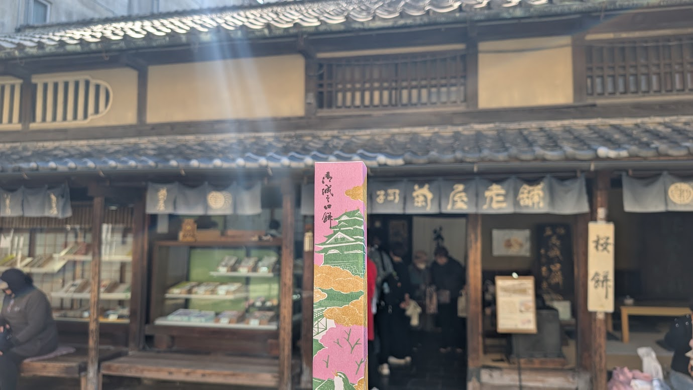本家菊屋で購入した「御城之口餅（おしろのくちもち）」の六個入りパック（800円）。きな粉がまぶされた小さなお餅が並んでおり、横には説明書きの紙と楊枝が添えられている。