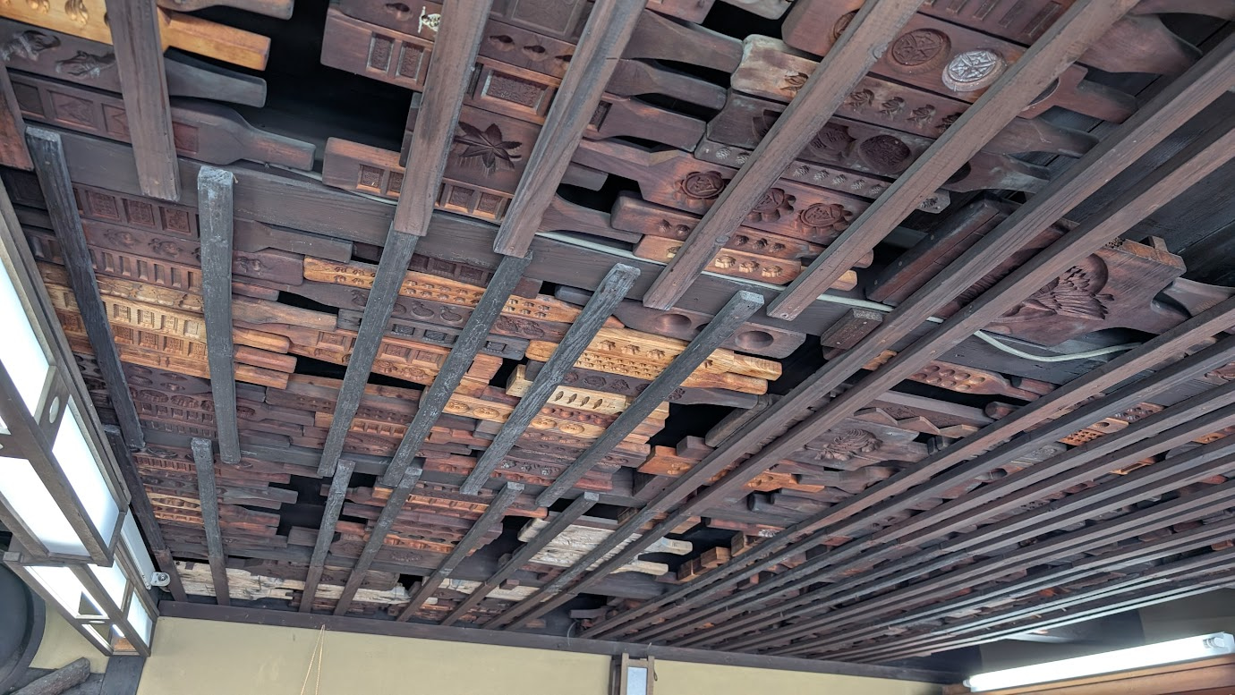 本家菊屋の店内の天井付近。天井の梁や壁一面に、無数の古い菓子型（木型）がびっしりと収納されており、圧倒的な歴史の厚みを感じさせる。