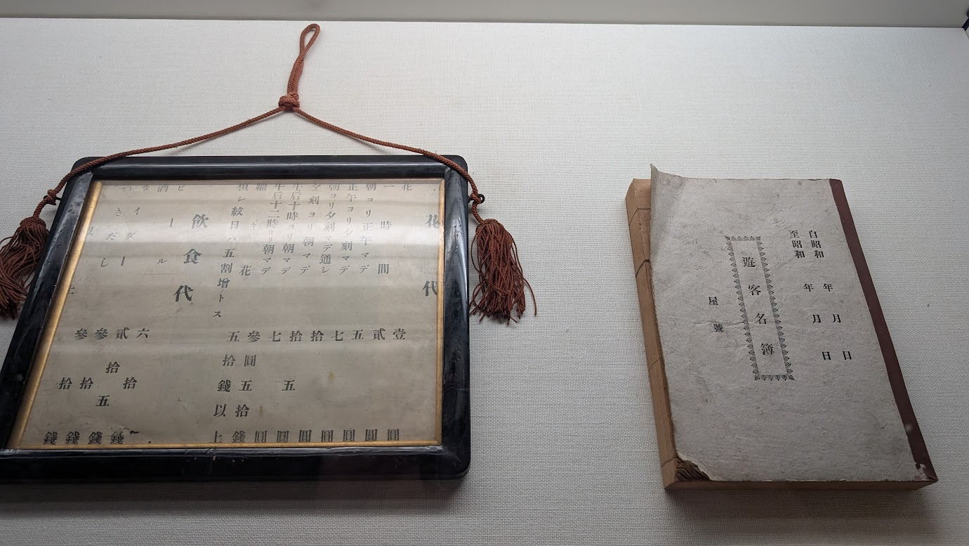 奈良県大和郡山市の町家物語館に展示されている、当時の「遊客名簿」と「飲食代・花代」の料金表。時間帯ごとの詳細な利用料金が古い文字で記されている。