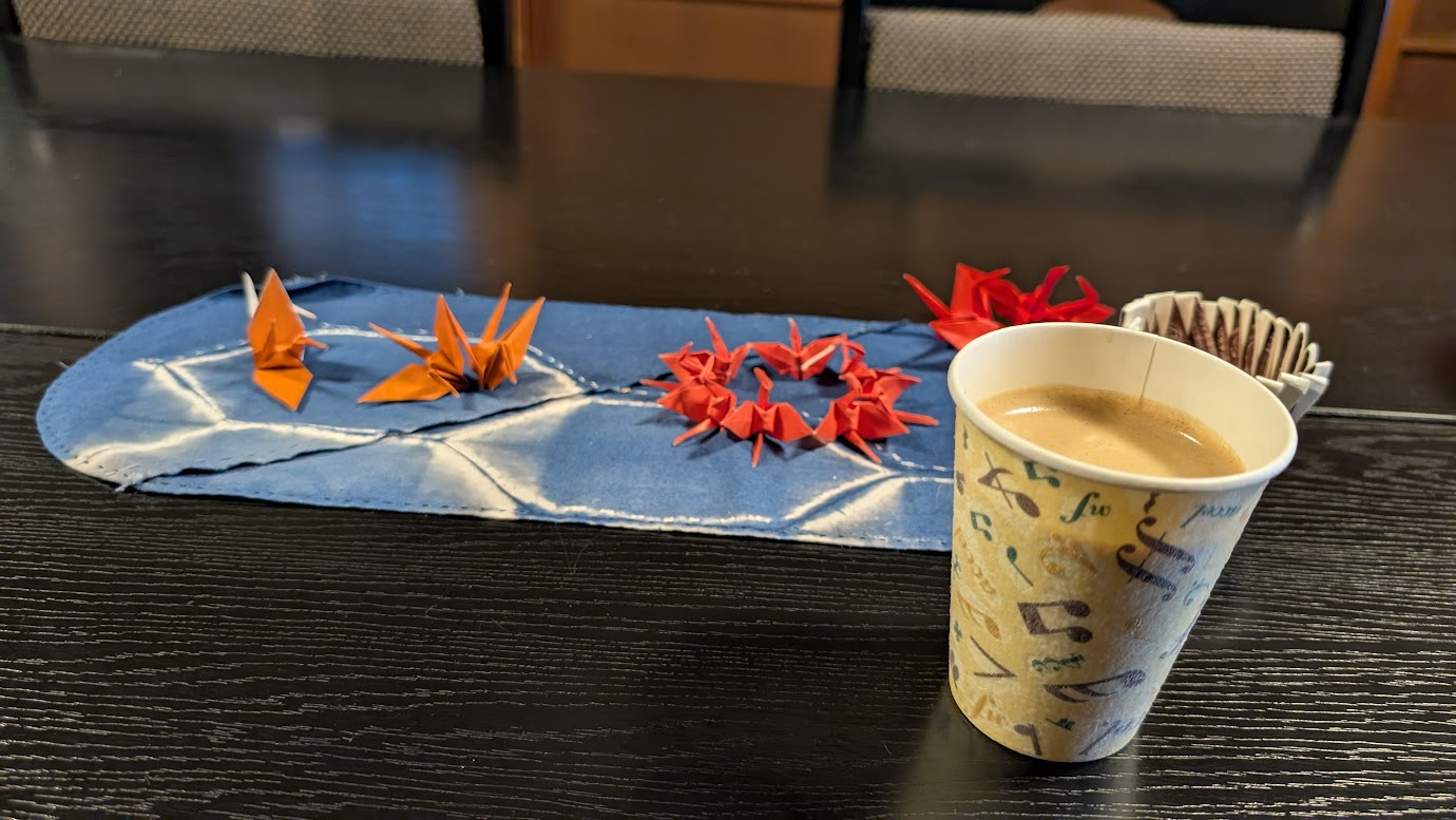 奈良県大和郡山市の町家物語館にある喫茶コーナー。100円コーヒーと、テーブルに飾られた色鮮やかなオレンジと赤の連鶴（折り鶴）が写っている。