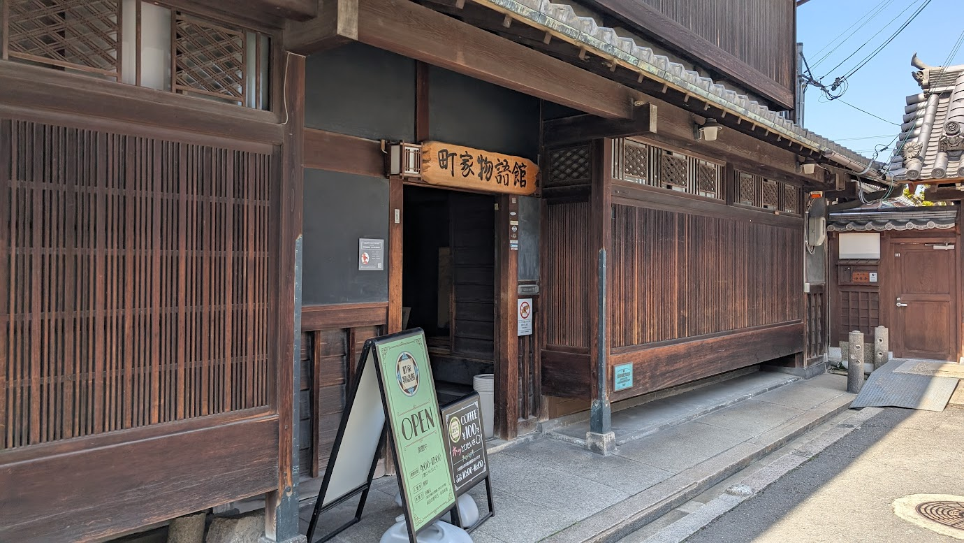 奈良県大和郡山市にある町家物語館（旧川本家住宅）の入口。大正・昭和初期に遊郭として使われていた、重厚な木造3階建ての建築で、格子戸の前には提灯が下がり、軒下には花が飾られている。