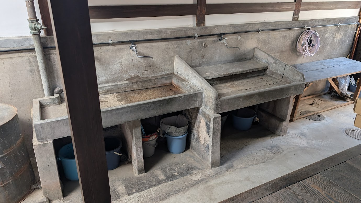 奈良県大和郡山市の町家物語館（旧遊郭建築）にある、古い石造り（コンクリート製）の流し台。蛇口がいくつか並び、台の下にはバケツなどが収納されている。