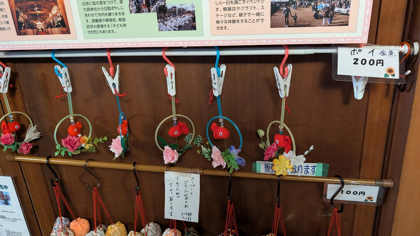 奈良県大和郡山市の町家物語館で販売されている「ポイ金魚」。金魚すくいのポイの枠の中に、赤い布製の金魚と色鮮やかな造花が飾られた吊るし飾り。