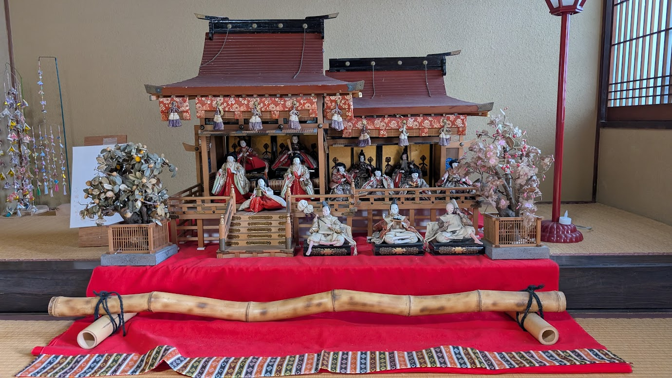奈良県大和郡山市の町家物語館に展示されている、昭和10年頃に購入された御殿飾りの雛人形。赤い毛氈の上に、精巧な木造の御殿と多くの雛人形が並んでいる。