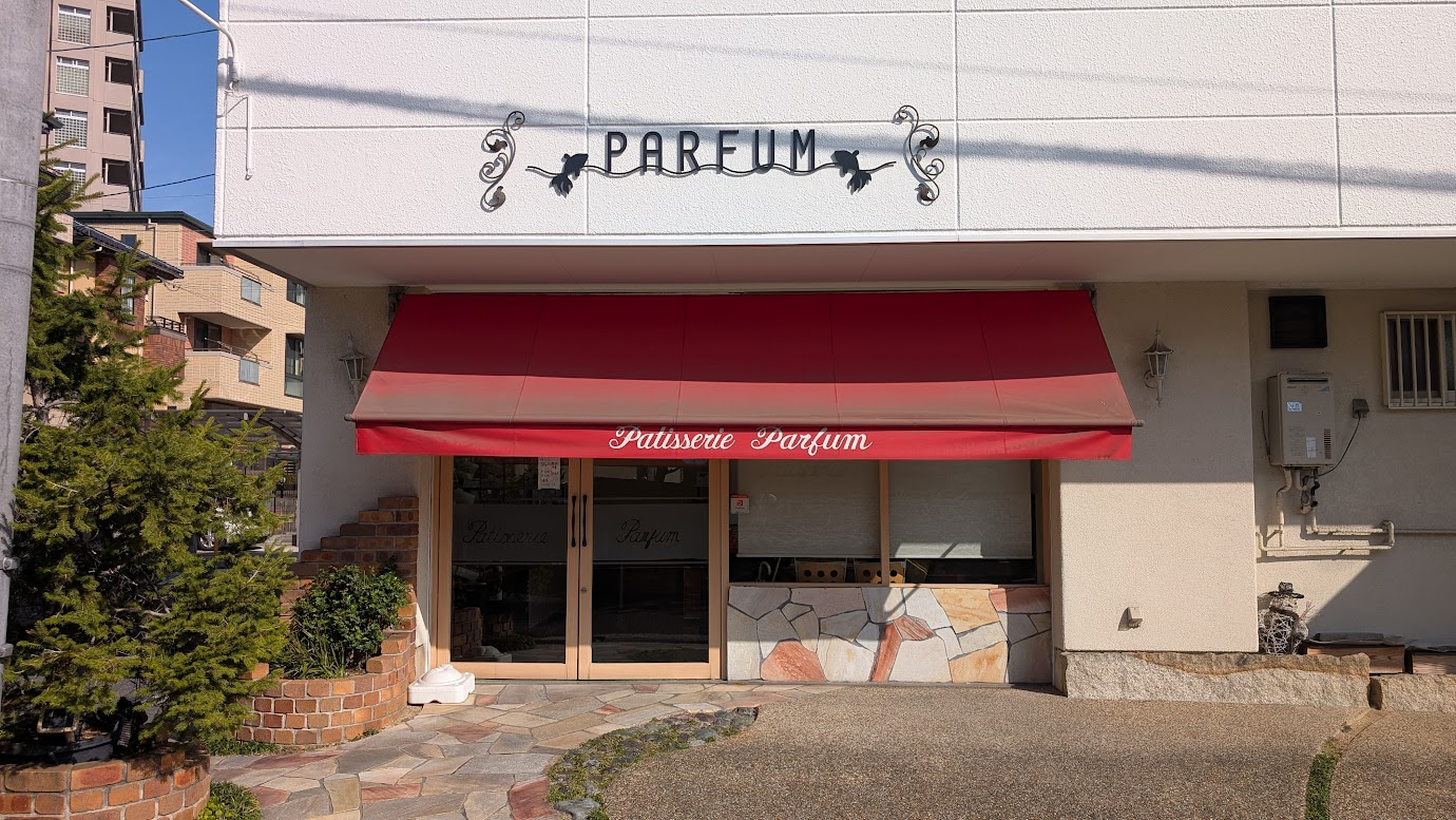 奈良県大和郡山市にある手作り洋菓子専門店「パルファン」の外観。レンガ造りのアットホームな建物で、赤い看板が掲げられ、店先にはおもてなしのベンチが置かれている。