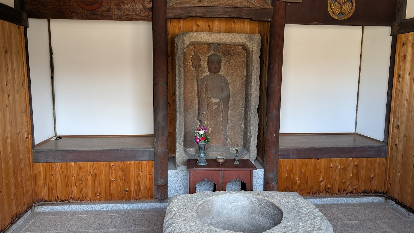 奈良県大和郡山市の洞泉寺にある「垢かき地蔵」。石造りの祠の中に彫られた地蔵菩薩像の全身が写っており、手前には供えられた花と石の鉢が置かれている。