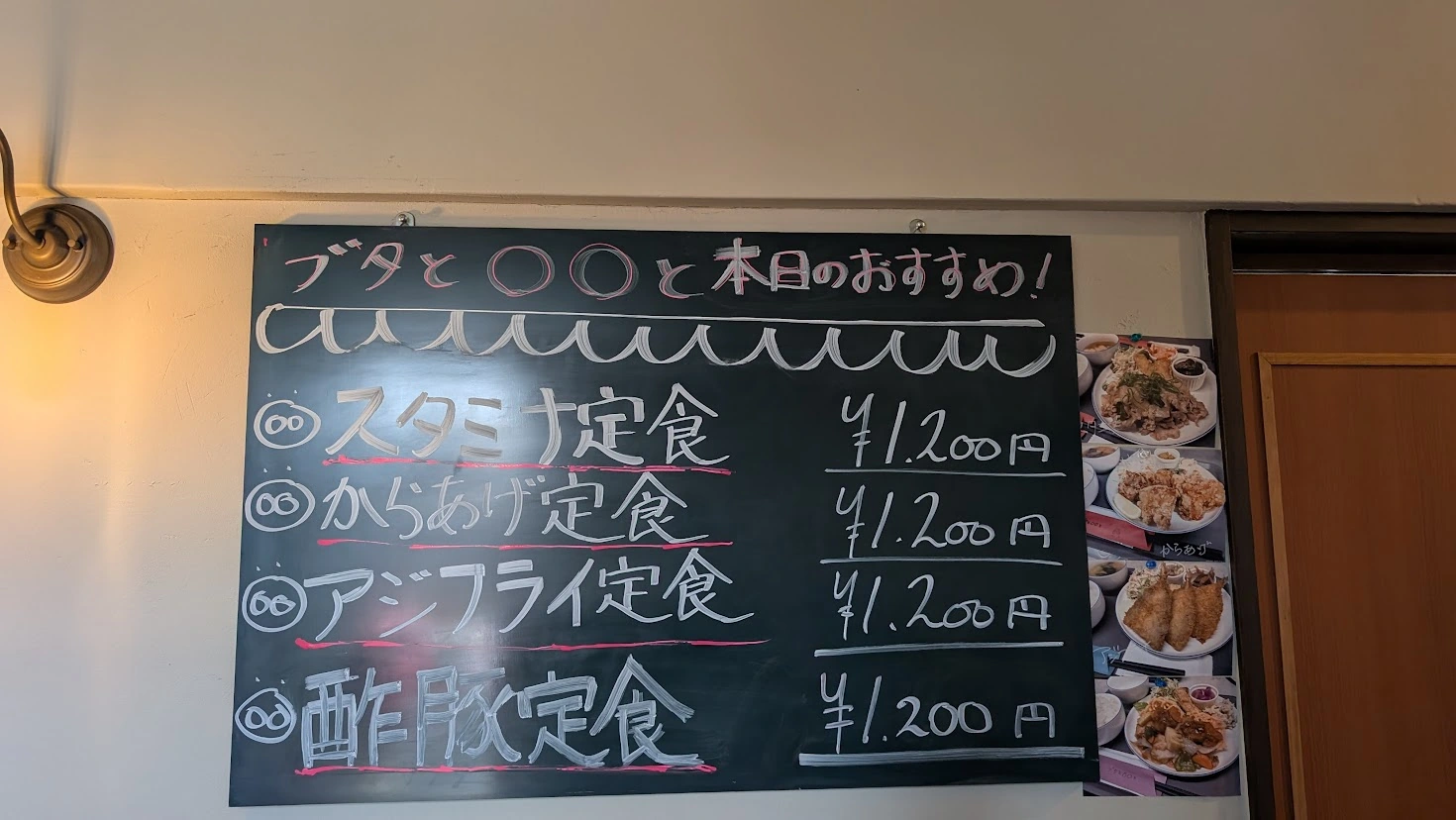 「工場内食堂 ぶたと〇〇と。」のレジ横にある黒板メニュー。スタミナ定食、からあげ定食など、本日のおすすめ定食が手書きで案内されている風景。