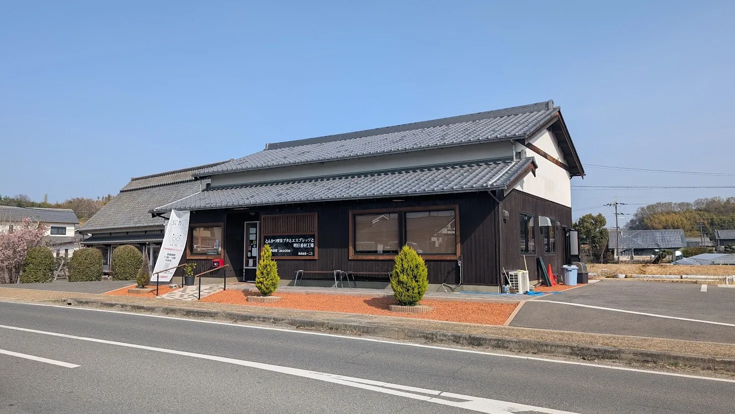 明日香村にある「工場内食堂 ぶたと〇〇と。(とんかつ喫茶ブタとエスプレッソと 明日香村工場)」の外観写真。黒い木目調の外壁に瓦屋根を乗せた和風の平屋建ての店舗風景。