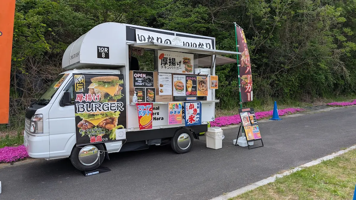 葛城市の芝桜まつり会場に停車している白いキッチンカー。「厚揚げBURGER」と書かれた大きなタペストリーやメニューが掲示されている風景