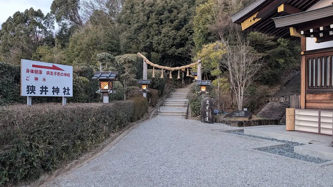 大神神社の境内に立つ狭井神社への案内看板。矢印の先に木々に囲まれた静かな参道が続いている風景。