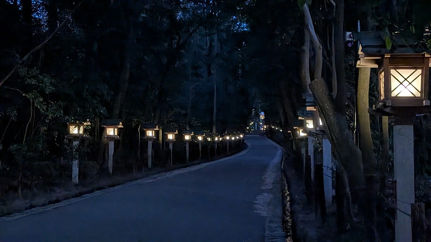 夕暮れ時、左右に等間隔で灯籠が並び、明かりが灯った大神神社の静かな参道。