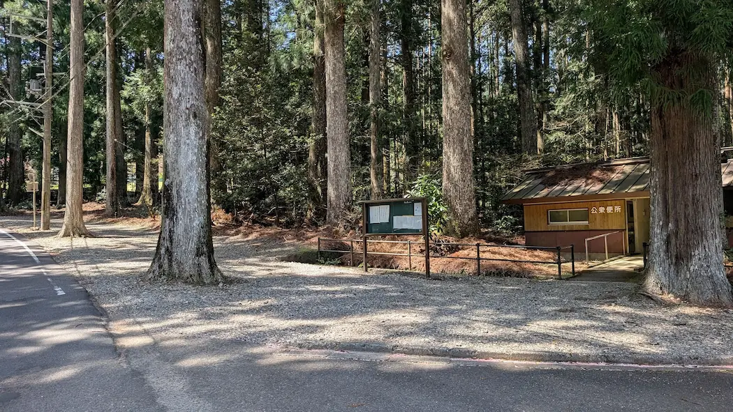 奈良県下北山村、池神社の駐車場。杉の巨木に囲まれた砂利敷きの駐車スペースと、隣接する木造の公衆トイレの様子。