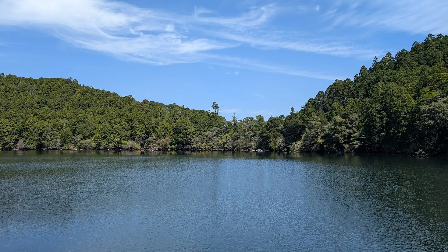 奈良県下北山村にある明神池の全景。周囲を深い山々に囲まれ、穏やかな水面に空と緑が鮮やかに映り込んでいる美しい風景。