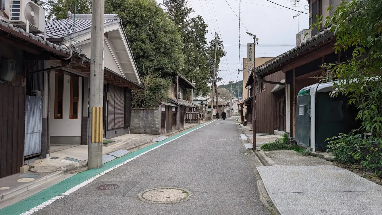 奈良県宇陀市、宇太水分神社の入り口付近の風景。細い一方通行の道の左手に神社の鳥居と、参拝者用の駐車場入り口が見えている様子。