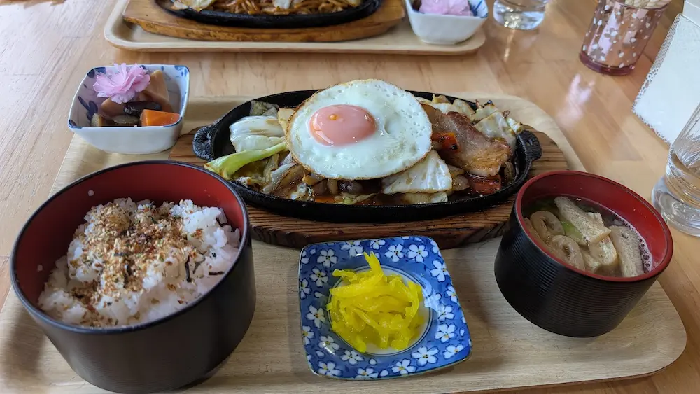 Open cafe 秀（しゅう）の、鉄板に乗った目玉焼き付き野菜炒め定食。ふりかけご飯とお味噌汁、小鉢のセット