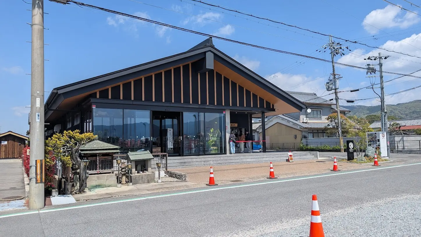 奈良県桜井市にある「肉のカワイ」の店舗外観。黒い大きな屋根とガラス張りのモダンな平屋建てで、手前にはアスファルトの道路と赤いカラーコーンが並んでいる風景