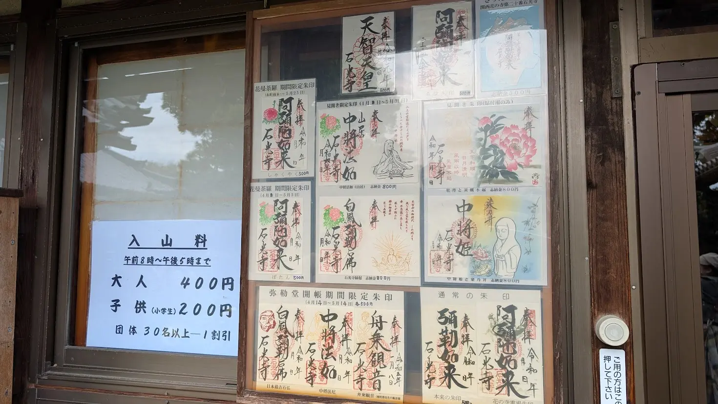 奈良・石光寺の受付窓口。左側に入山料（大人400円、子供200円）の案内があり、右側には中将姫や季節限定の牡丹のイラストが入った多数の御朱印サンプルが掲示されている風景