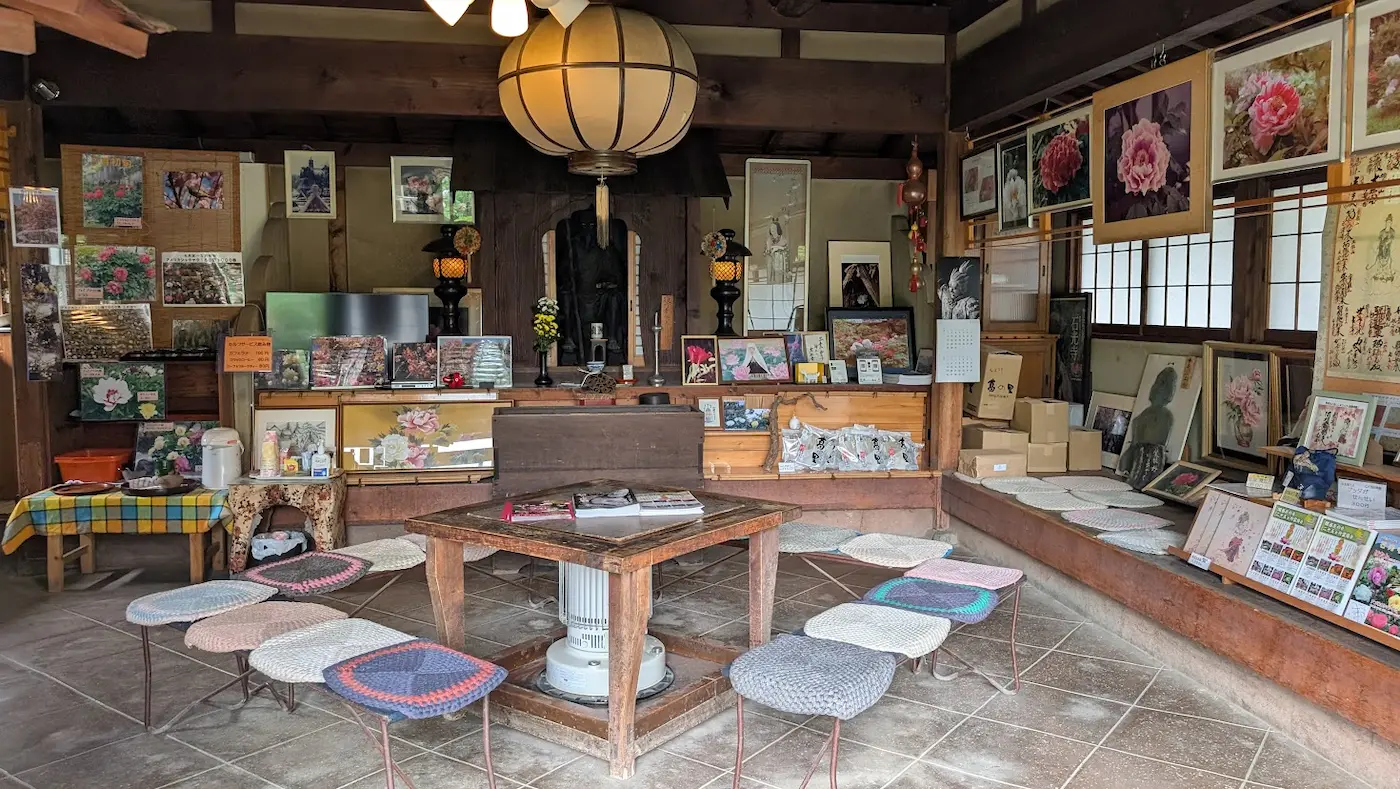 奈良・石光寺の休憩室内部。壁一面に牡丹の写真やポスターが飾られ、中央には木のテーブルと丸い手編みの座布団が並んだ椅子がある、どこか懐かしい和の空間