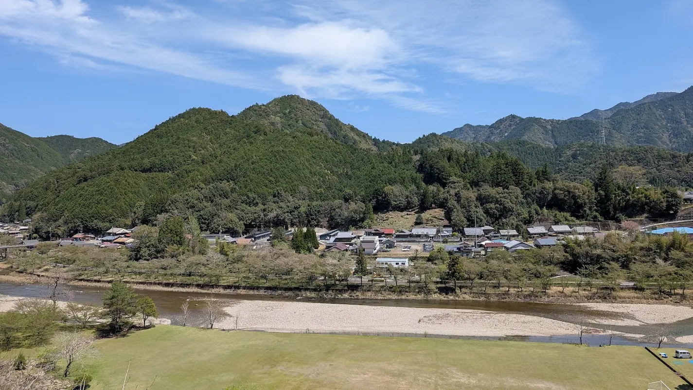 下北山村ののどかな集落の風景と、背後にそびえ立つ池原ダムの巨大なアーチ堤体