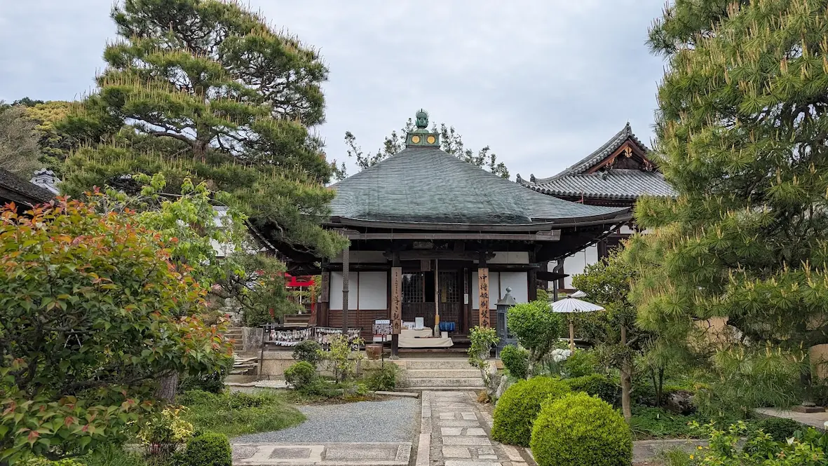 奈良・當麻寺の中之坊にある、寄棟造の「中将姫剃髪堂」。手前には整えられた石畳の参道があり、左右を立派な松や新緑の木々、庭園の緑が囲んでいる風景