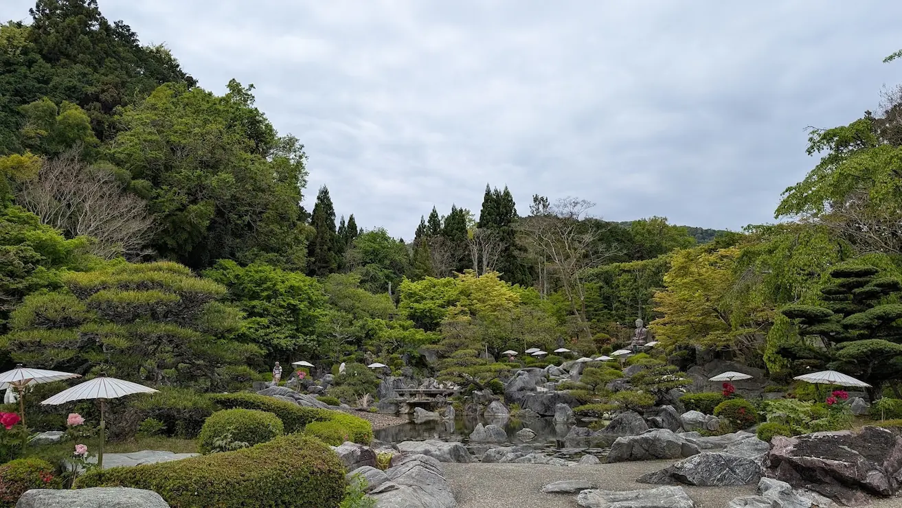 奈良・當麻寺奥院の浄土庭園。手前に整えられた芝生と和傘、中央に大きな池と石組み、背景には深い緑の山々と新緑の木々が広がる広大な風景