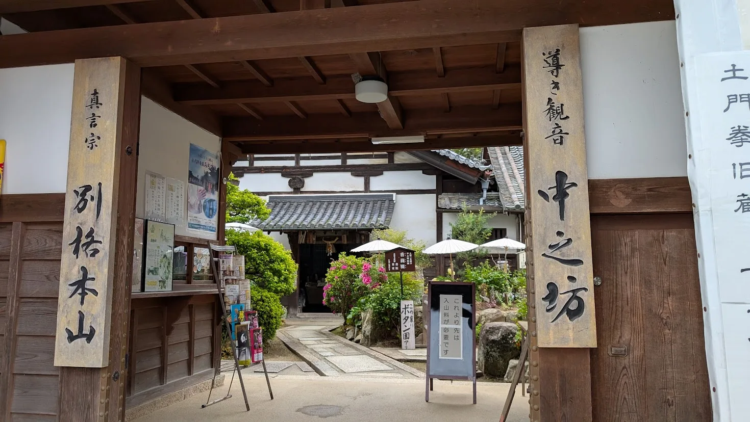 奈良・當麻寺の中之坊の入り口。右側に「中之坊」、左側に「別格本山」と書かれた大きな木製看板があり、門の奥には白い和傘と咲き誇る牡丹、美しい庭園の一部が見える風景