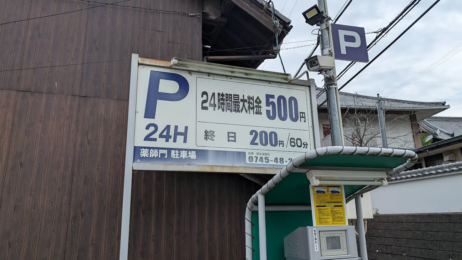 當麻寺の「薬師門駐車場」の看板。終日60分200円、24時間最大料金500円と記載されている。横には精算機が設置されている風景