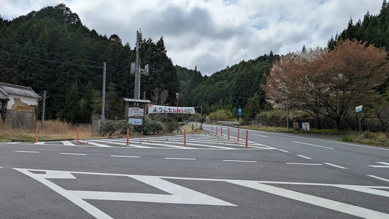 宇陀・弁財天へ続く最終分岐点。左側に「ようこそ石楠花の丘へ」の横断幕と案内板があり、赤いポールで仕切られたＴ字路の風景