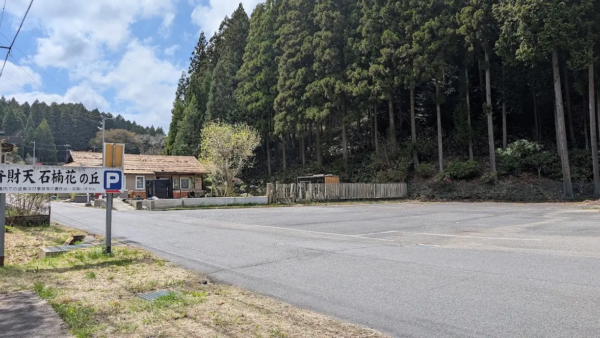 奈良・宇陀の弁財天（石楠花の丘）にある、広く舗装された平面駐車場。入口には「弁財天 石楠花の丘 P」と書かれた看板があり、背景には杉林が広がっている