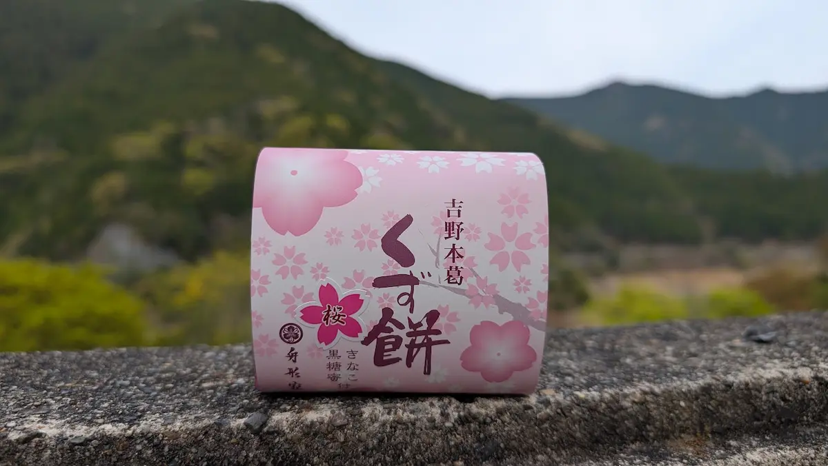 下北山村の山々を背景に、石垣の上に置かれた奈良名産「吉野本葛 くず餅」の桜色パッケージ