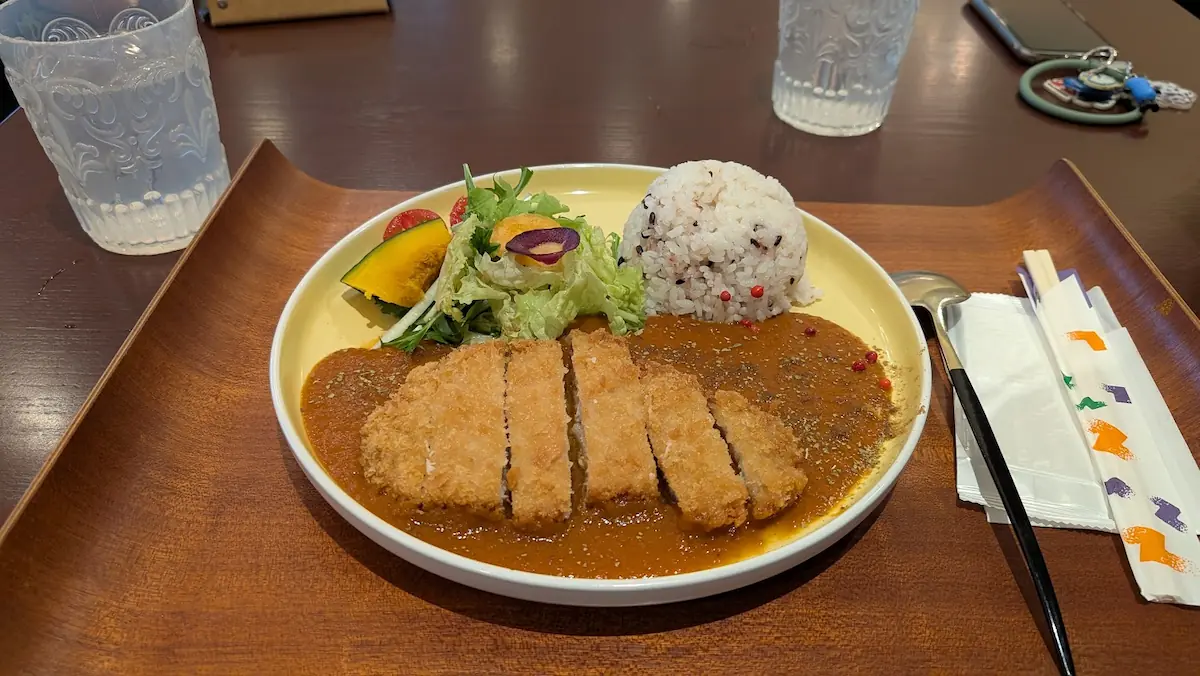 黄色のプレートに盛り付けられた、厚切りのカツとサラダが添えられたカツカレーの全体写真