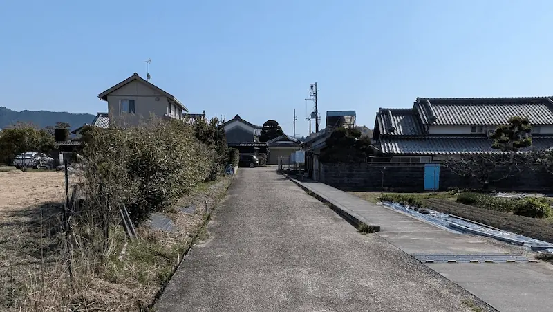 明日香村の直売所「あすか夢の楽市」から飛鳥寺へ向かう道。舗装された細い生活道路が続き、左右には畑や民家が広がるのどかな風景。