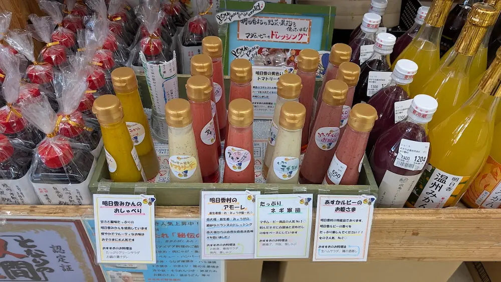 明日香村の特産品を使ったバラエティ豊かなドレッシングの陳列。黄色、赤、白など色鮮やかなボトルと、それぞれの特徴やおすすめの食べ方が書かれた手書きのポップ。